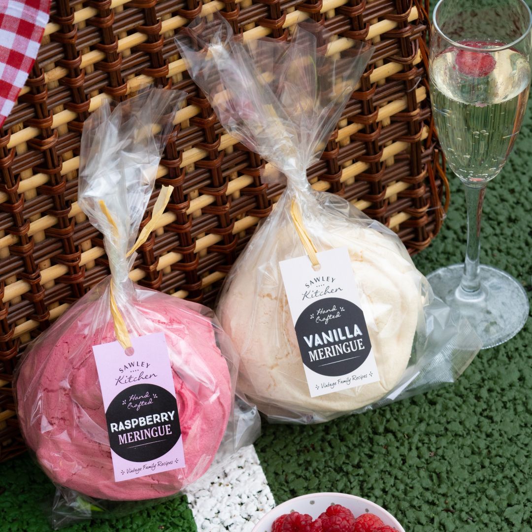 Two wrapped meringues labeled 'Raspberry' and 'Vanilla' next to a glass of champagne