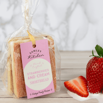 Packaged strawberries and cream shortbread with a pink tag on a wooden surface with strawberries.