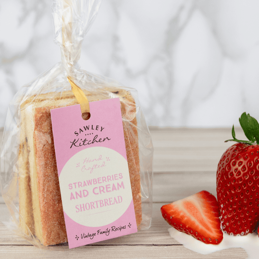 Packaged strawberries and cream shortbread with a pink tag on a wooden surface with strawberries.