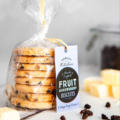Packaged Fruit Shrewsbury Biscuits in a clear plastic bag with a label showing the brand and product name, along with some loose biscuits and dried currants on the table.