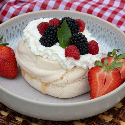 Vanilla meringue dessert with whipped cream and berries on a plate with a checkered cloth background