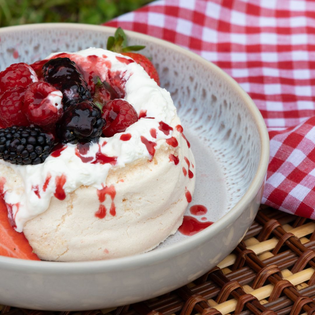 Dessert with vanilla meringue, berries, and drizzle in a white bowl on a checkered tablecloth.